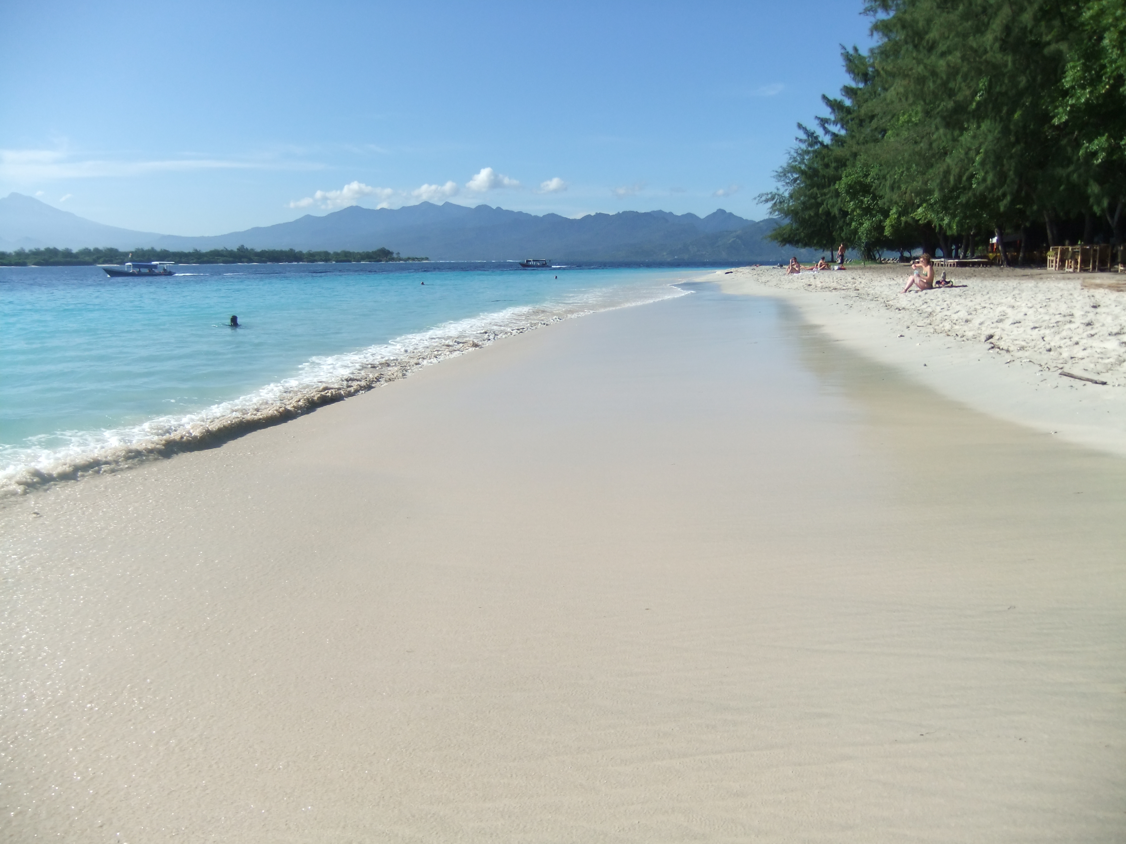 Pale sand and turquoise shallows on Gili Trawangan's beach, with traditional fishing boats moored near the reef