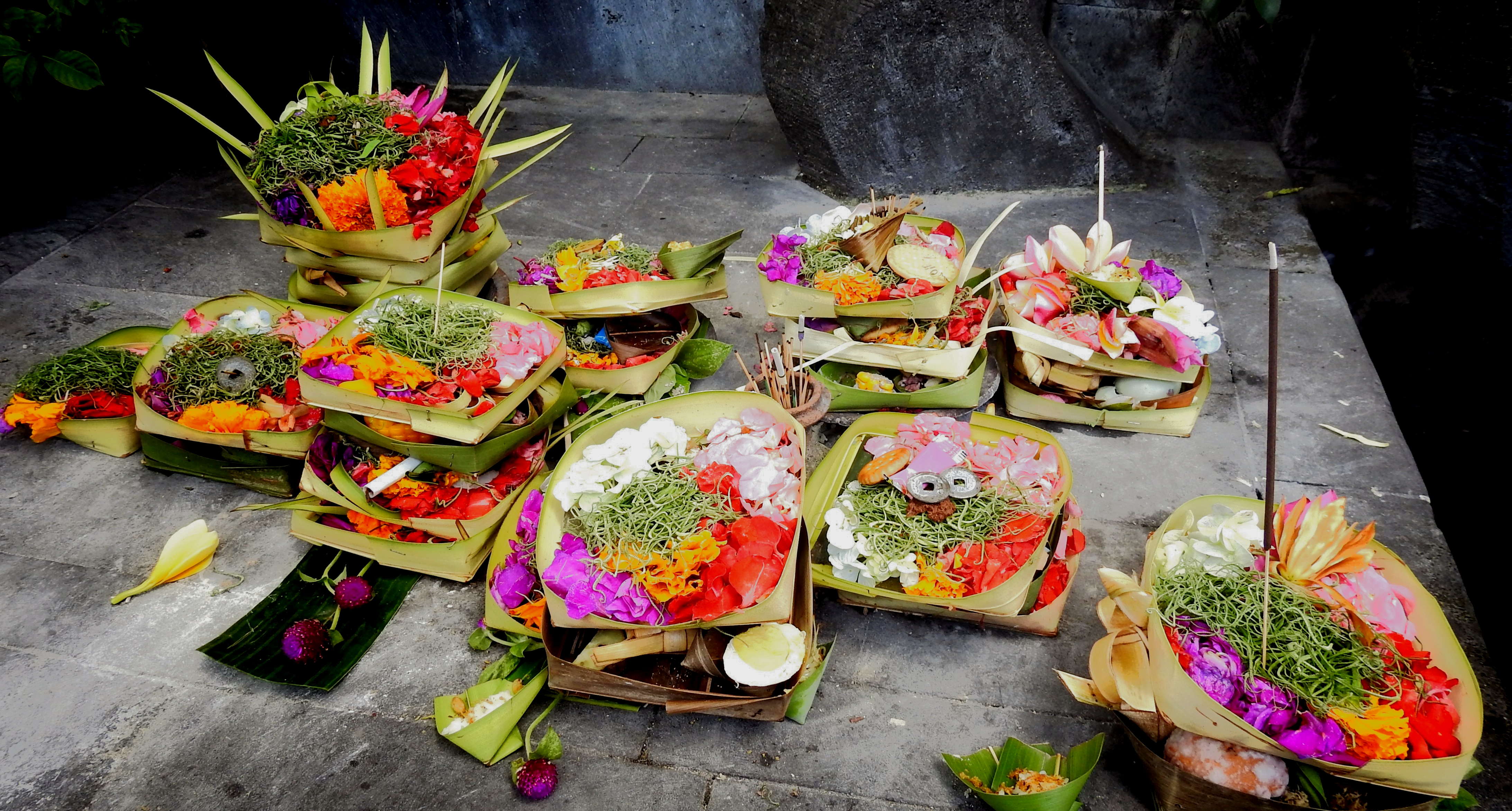 Close-up of a canang sari offering with flowers and incense