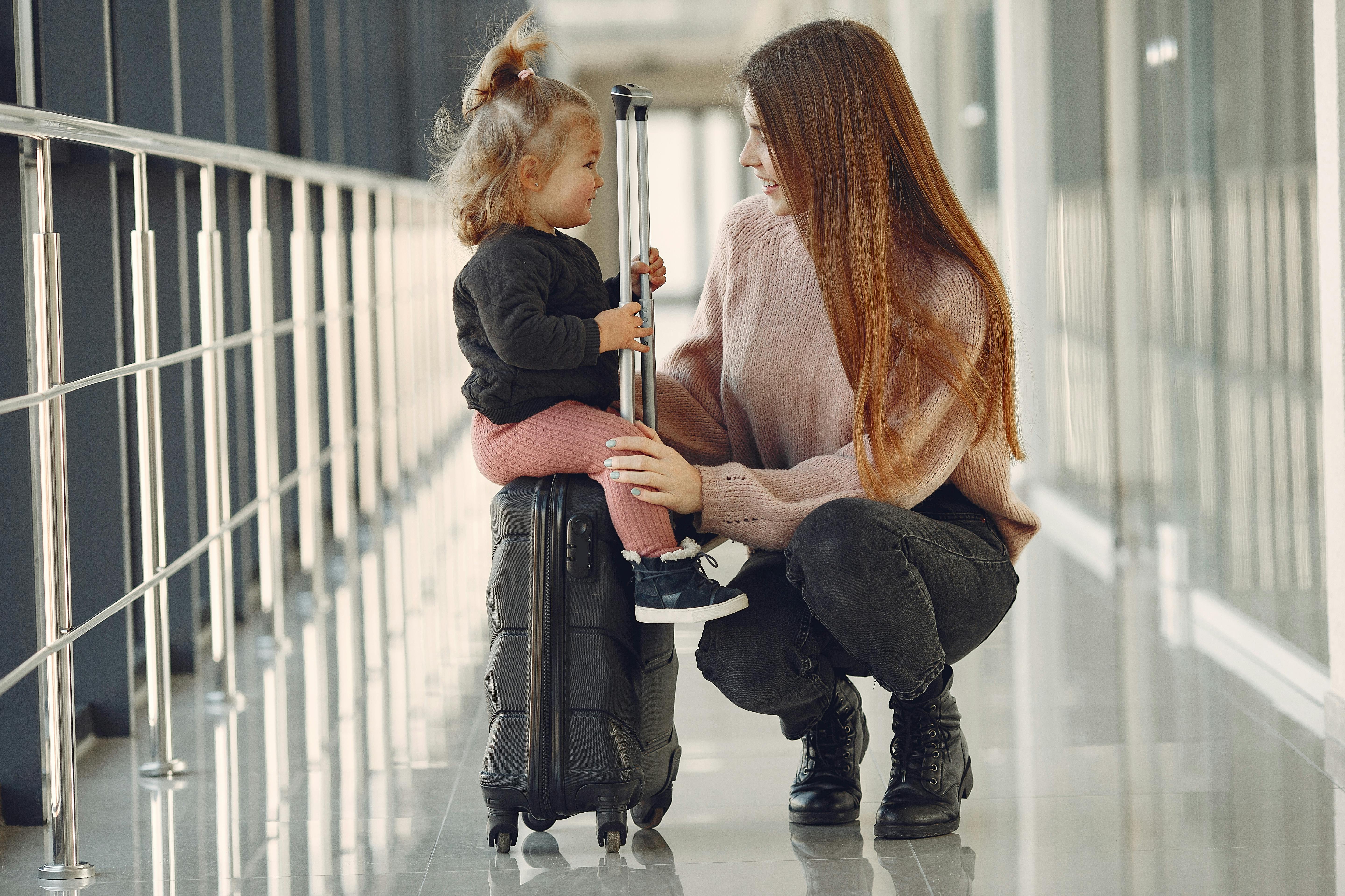 Mother and young child waiting at an airport with a suitcase