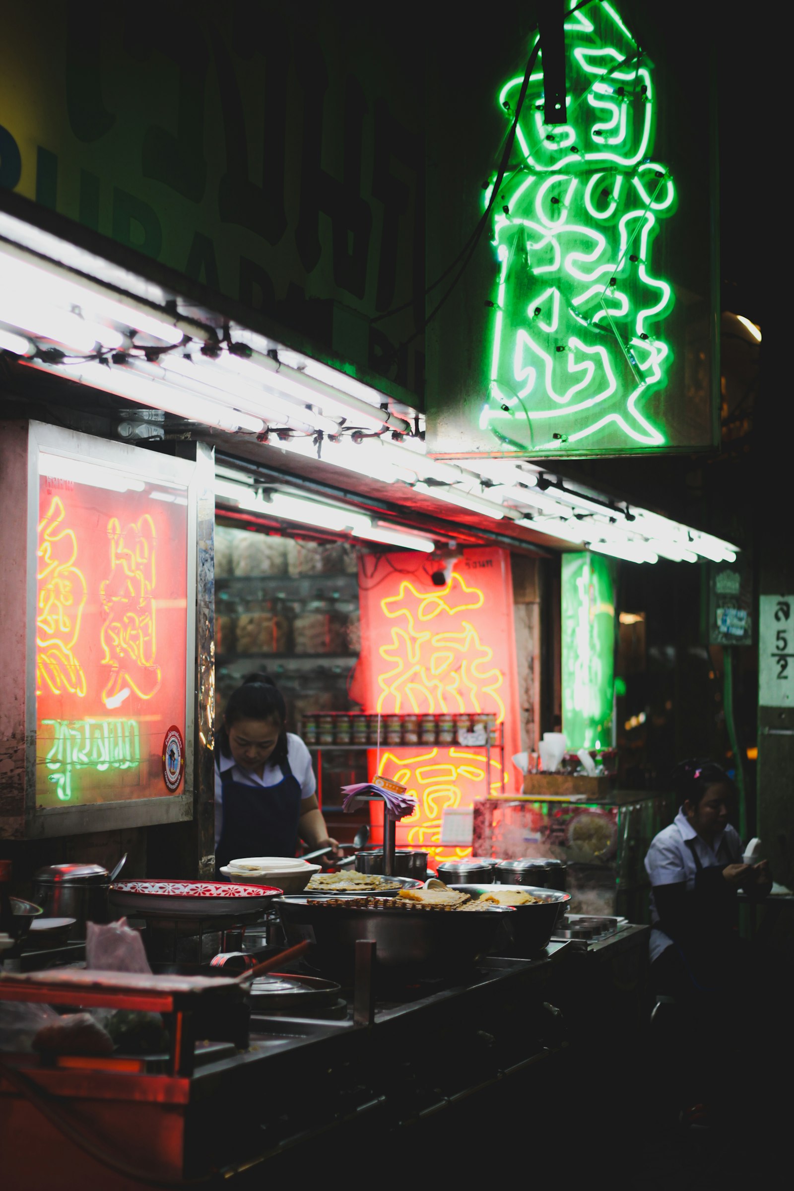 Street food stall lit by neon signs at night