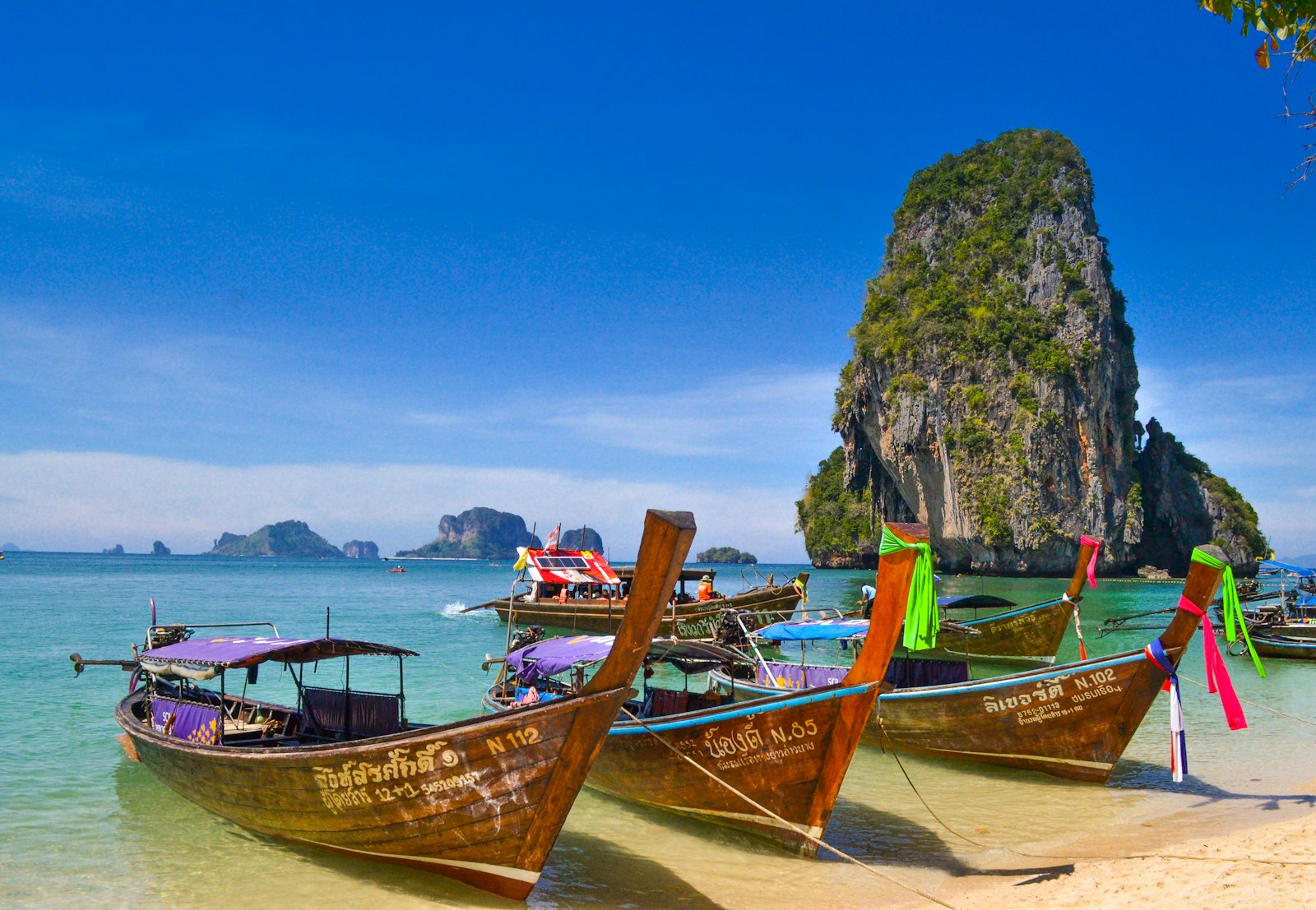 Longtail boats on a Krabi beach below limestone cliffs