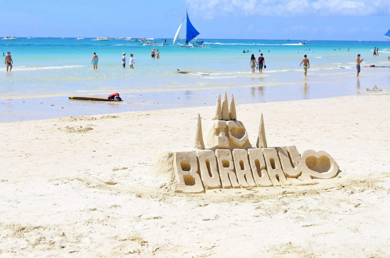 People walking along Boracay's White Beach with shoreline restaurants visible — the postcard beach with the matching price tag